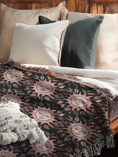 Luxurious woven cotton throw featuring dreamy blush pink sun faces with closed eyes against black background with delicate ray patterns and elegant fringe trim. Perfect celestial wall hanging, witchy bedroom decor, or dark academia throw blanket.